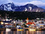 Yachts docked on waterfront, city & mountains.