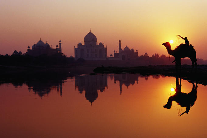 Taj Mahal & silhouetted camel & reflection in Yamuna River at sunset.