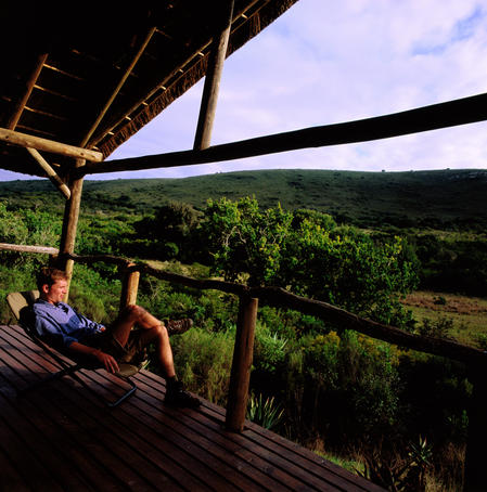 Man relaxing on hotel balcony and looking over grasslands.