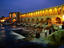 People sitting on the steps of an illuminated Khaju Bridge at night.