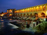 People sitting on the steps of an illuminated Khaju Bridge at night.