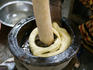 Fufu (mix of steamed plantains and cassava root) being pounded using a wooden bowl and long stick.