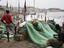 Fisherman mending nets with boats and town in background.
