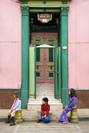 Children sit in front of a colourful house in hillside of city.