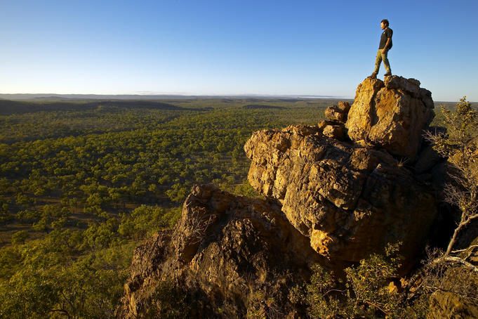 Man looking over savannah country from rocky outcrop.