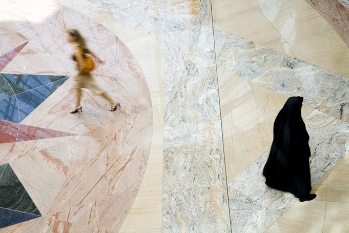 Overhead of Muslim woman dressed in abaya and hijab (black robe and scarf) passing woman dressed in western attire at Mall of the Emirates.