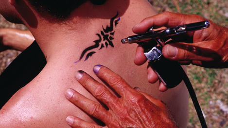 Young man getting spray-on tattoo in Lummus Park at South Beach.