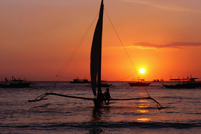 Paraw (traditional outrigger sailboat) sailing at sunset.
