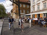 Cyclists passing outdoor cafes along river.