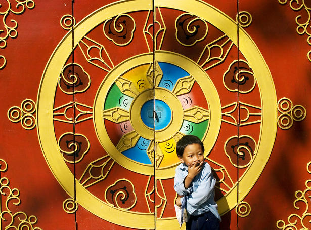 Boy in front of ornate monastery gates.
