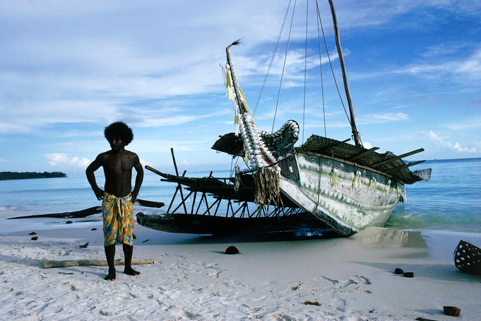 Man stands next to traditional trading canoe, Trobriand Islands.