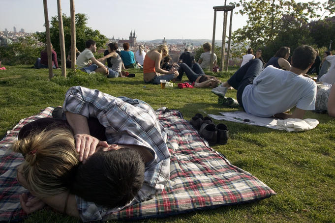 People on grass enjoying view over city from beer gardens, Letna Park with couple cuddling in foreground.