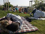People on grass enjoying view over city from beer gardens, Letna Park with couple cuddling in foreground.