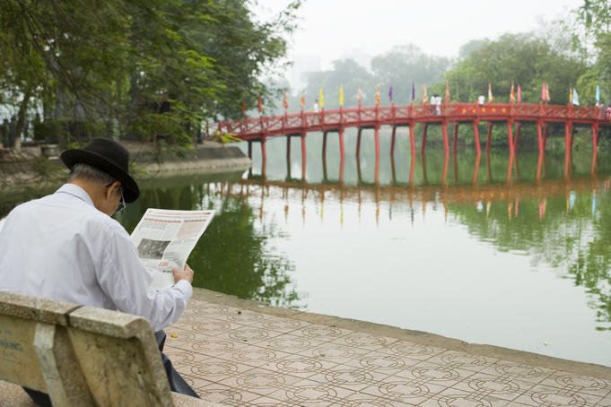 Man reading paper beside The Huc Bridge on Hoan Kiem Lake.