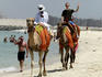 Camel and tourists on Jumeriah Beach with the new construction of the Palm Island in the background.