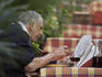 Man reading newspaper while dining on pasta and red wine.