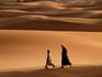 Men walking across sand dunes.
