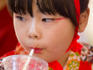Young girl dressed in traditional kimono drinking from a straw.