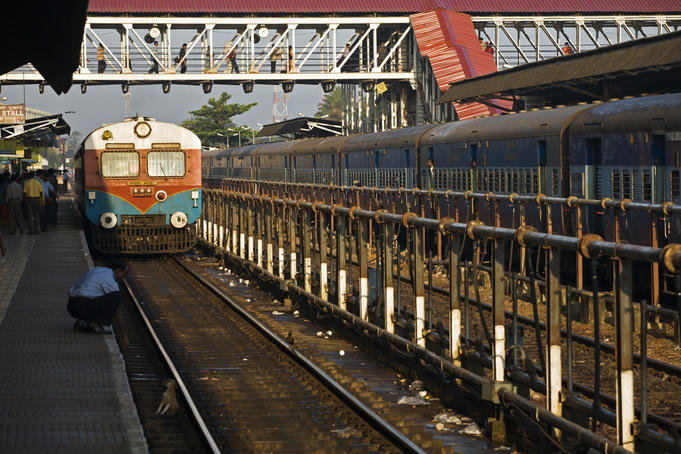 Man helping a puppy off the tracks as a train approaches, Margaon railway station.