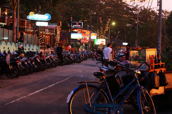 Line of motorbikes and street vendor at sunset.