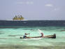 Man paddling while another man bales water out of wooden boat in open water.