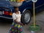 Woman carrying vegetables in large metal bowl on head.