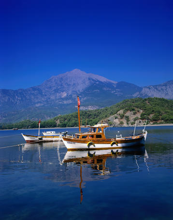 Boats moored on the pristine Mediterranean waters at Phaselis Cove south of Antalya. Mount Olympus is in the background.