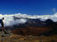 A lone hiker standing on rocks, admiring the view of a cloud dusted valley in the Haleakala National Park on Maui