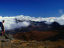A lone hiker standing on rocks, admiring the view of a cloud dusted valley in the Haleakala National Park on Maui