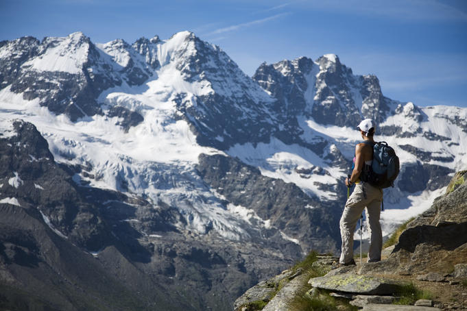 Hiker on traverse from Refugio Vitorio Sella to Herbetet with mountains of Gran Paradiso massif in background.