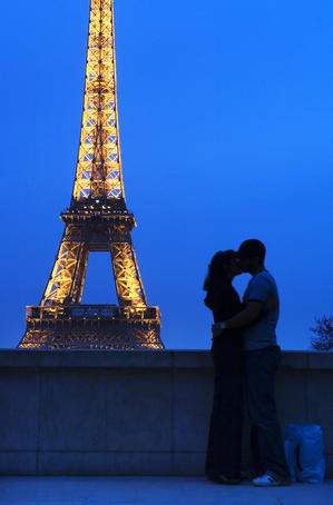 Lovers kissing in front of the Eiffel Tower at night.