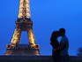 Lovers kissing in front of the Eiffel Tower at night.