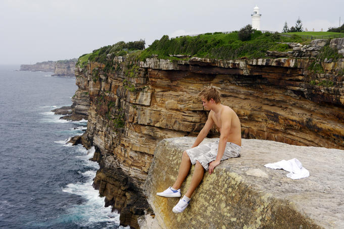 Young man sitting on edge of cliff at Vaucluse.