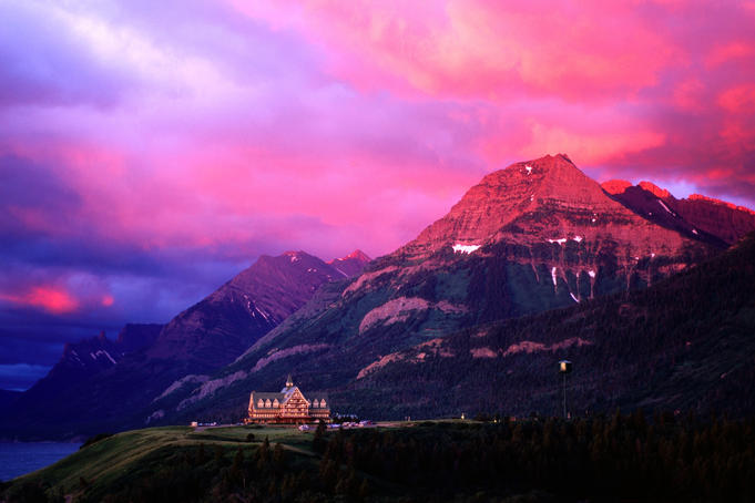 Prince of Wales Hotel and Canadian Rockies under a brilliant pink and orange-hued cloudy sky.