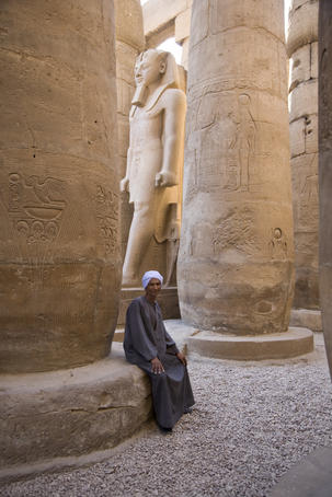Man sitting at the base of a column carved with hieroglyphs at Luxor Temple.