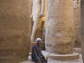 Man sitting at the base of a column carved with hieroglyphs at Luxor Temple.