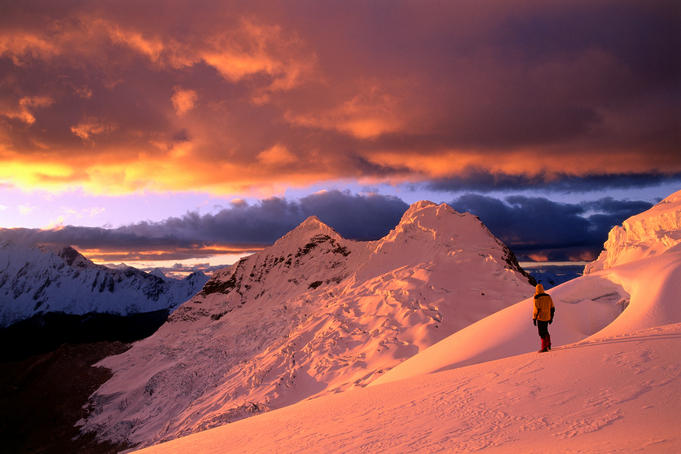 Climber on orange-tinted glacier above Ishinca Valley at sunset, Cordillera Blanca range.