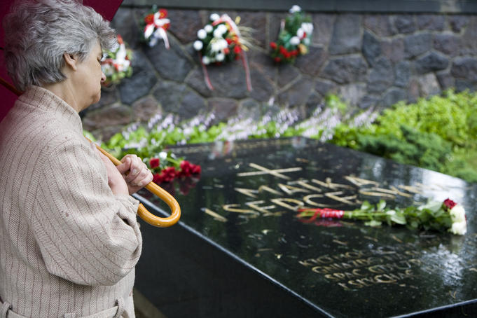 Woman in the rain under an umbrella visiting the black granite tomb of Polish military general and hero, Jozef Pilsudski, buried in Rasu Cemetery.