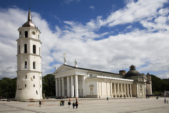 People gathering in front of Vilnius Cathedral and the belfry in old town Vilnius on a bright sunny day with puffy white clouds.