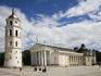 People gathering in front of Vilnius Cathedral and the belfry in old town Vilnius on a bright sunny day with puffy white clouds.