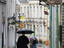 People with umbrellas strolling down narrow brick-laid street in old town Tallinn on rainy afternoon.