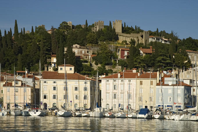 Boats in the harbour entrance with the old town walls on the hilltop in the distance.