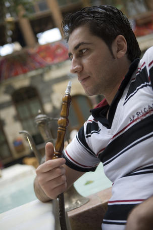 Man smoking sheesha water pipe, Jabri House courtyard restaurant.