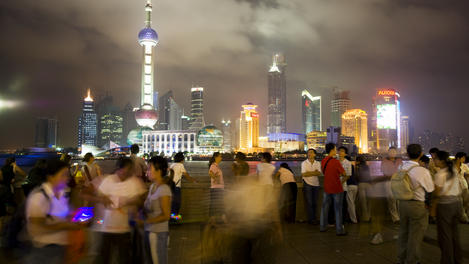 People socialising on the Bund promenade at night, with Pudong skyline in background.