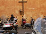 Wooden cross and parked scooters on busy street.