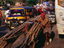 Man transporting bamboo poles on bicycle cart through town.