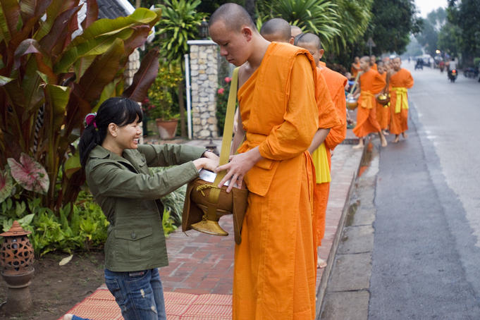 People giving alms (sticky rice) to monks during early morning procession on Thanon Sisavangvong street.