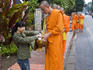 People giving alms (sticky rice) to monks during early morning procession on Thanon Sisavangvong street.