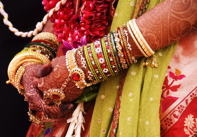 Bejewelled bride with henna hands at Mumbai wedding.