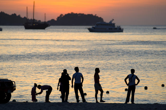 People on Patong Beach silhouetted at sunset.